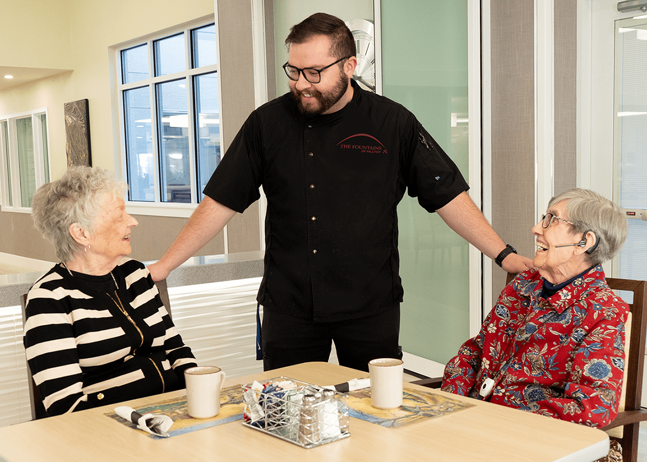 Chef greets two residents sitting down for a meal