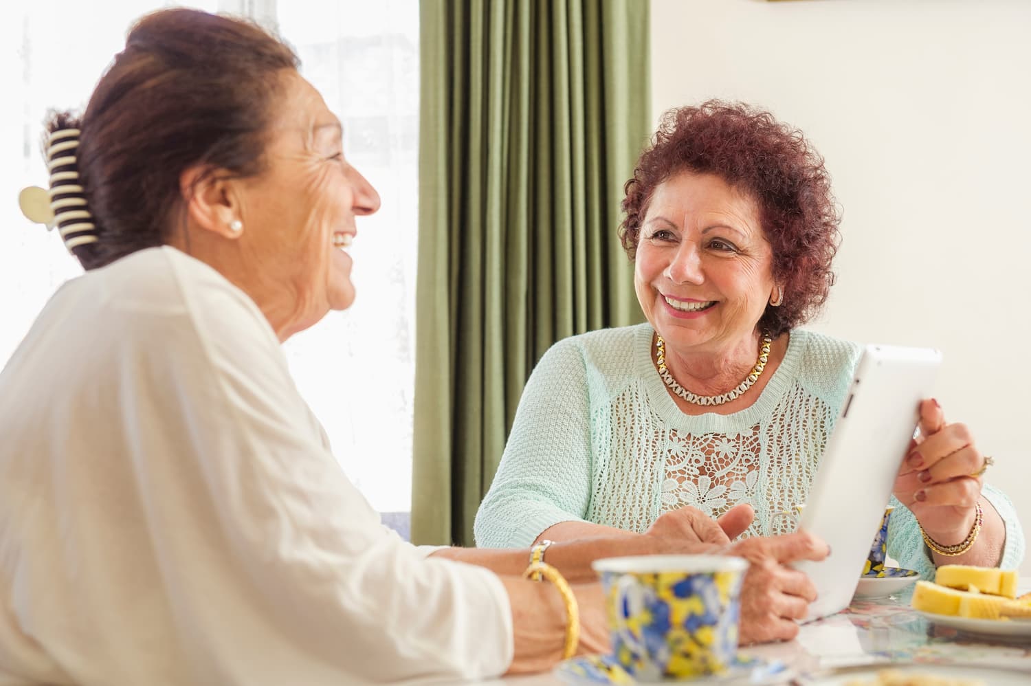 Two elders smiling and laughing drinking with tea cups on the table